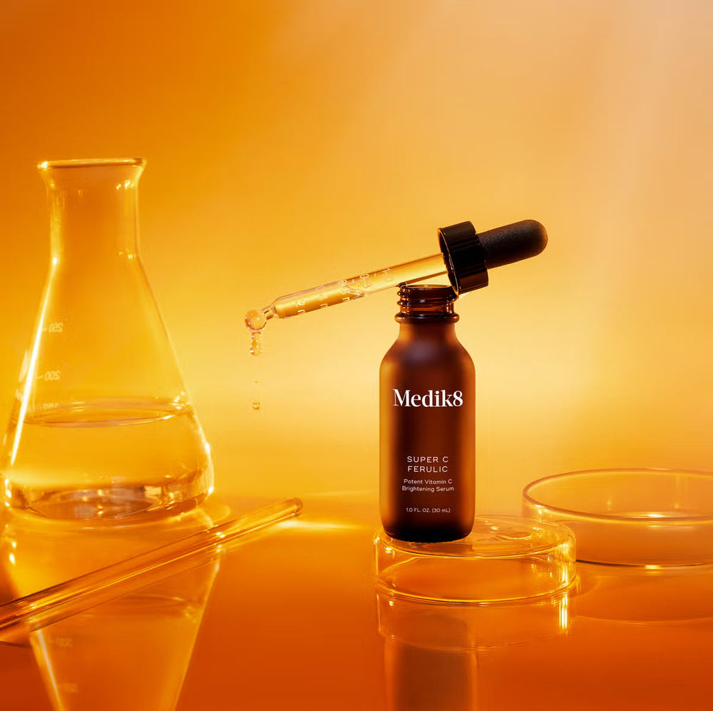 Medik8 vitamin C serum bottle with dropper against a warm orange background.