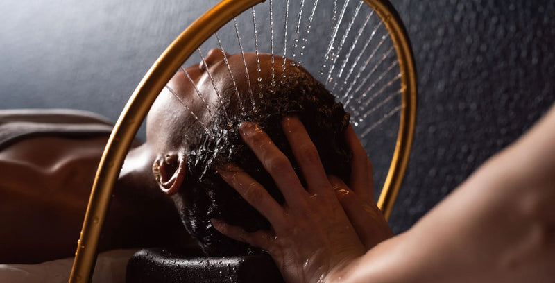 Relaxed woman receiving a head spa treatment in a salon, lying in a tub with a curved wooden frame over her head.